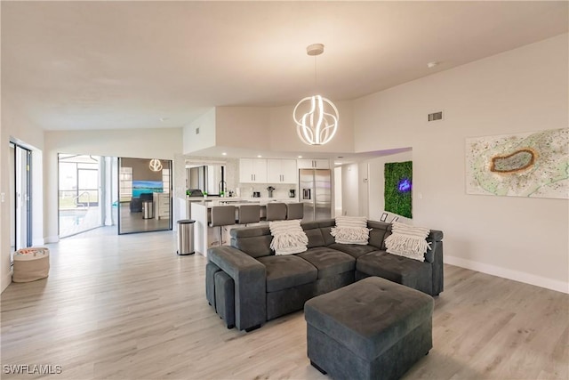 living area with visible vents, light wood-style flooring, an inviting chandelier, high vaulted ceiling, and baseboards