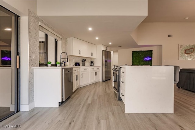 kitchen featuring light wood-style flooring, stainless steel appliances, white cabinetry, light countertops, and tasteful backsplash