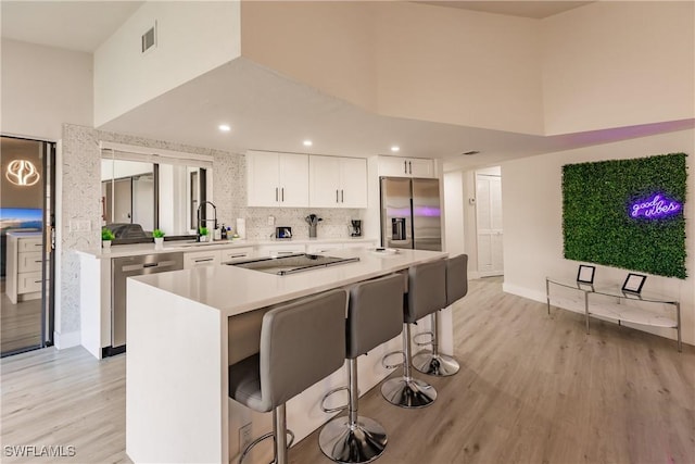 kitchen featuring a towering ceiling, light wood-type flooring, stainless steel appliances, and a sink