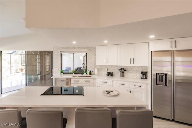 kitchen featuring light countertops, a sink, stainless steel refrigerator with ice dispenser, and black electric cooktop