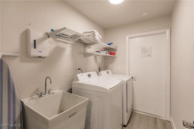 laundry area with light wood finished floors, laundry area, washing machine and dryer, and a sink