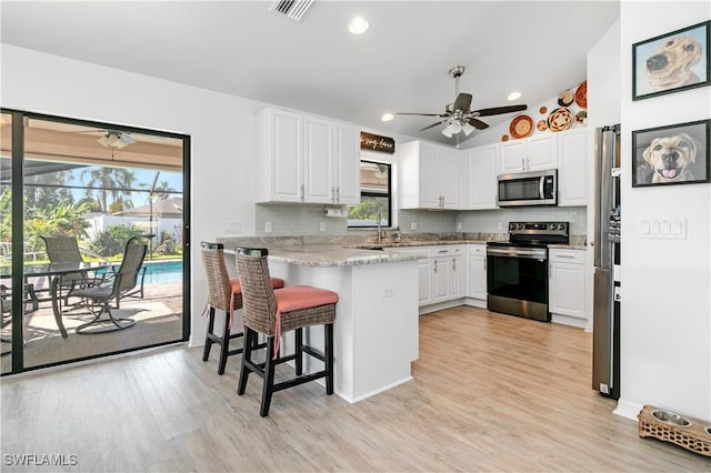 kitchen with white cabinets, kitchen peninsula, stainless steel appliances, and a breakfast bar area