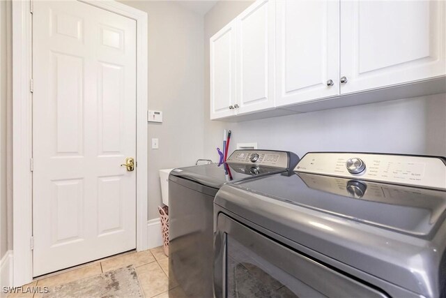 laundry room featuring cabinets, light tile patterned floors, and washing machine and dryer