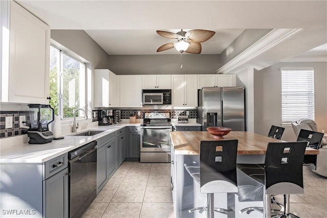 kitchen featuring wood counters, appliances with stainless steel finishes, a breakfast bar, gray cabinets, and white cabinetry