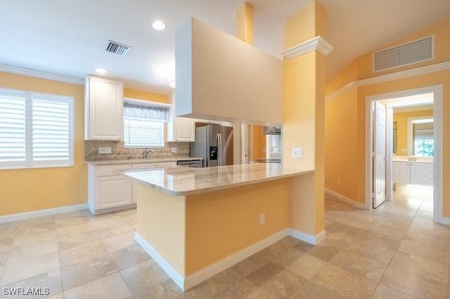 kitchen featuring kitchen peninsula, sink, stainless steel fridge, light stone counters, and white cabinetry