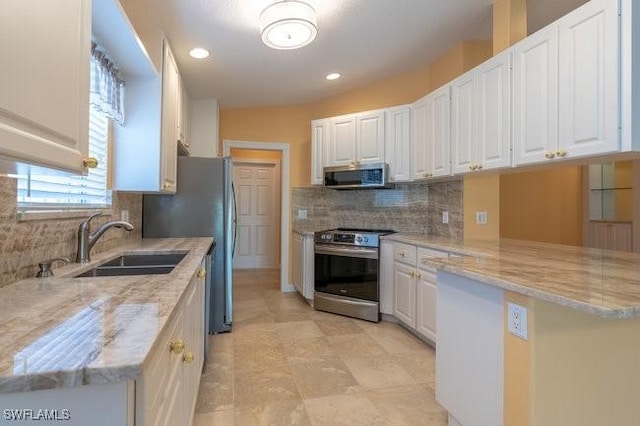 kitchen featuring kitchen peninsula, stainless steel appliances, white cabinetry, and light stone counters