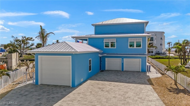 view of front of home featuring decorative driveway, fence, an attached garage, and metal roof