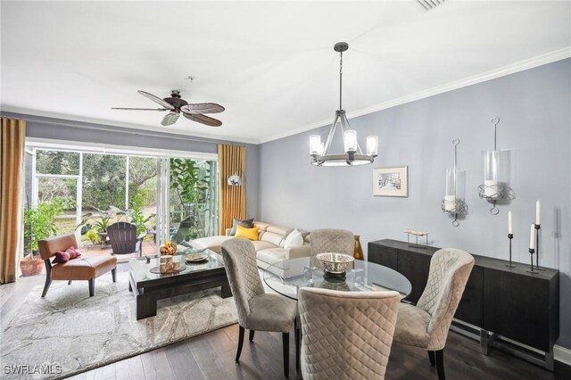 dining room with dark wood-type flooring, ceiling fan with notable chandelier, and ornamental molding