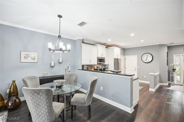 dining space featuring dark wood-type flooring, sink, ornamental molding, and an inviting chandelier