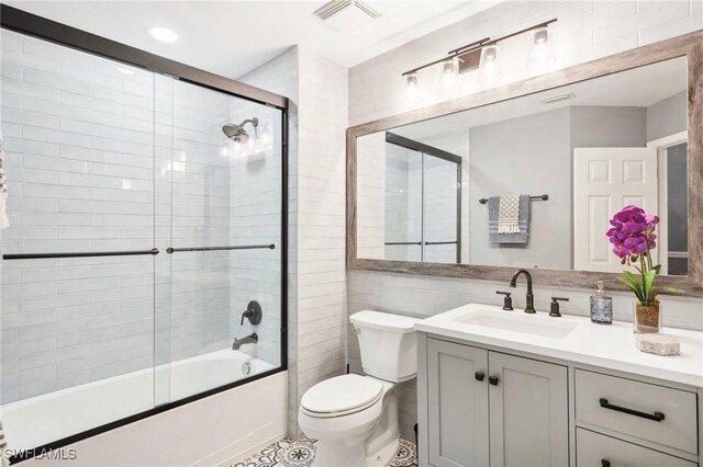 full bathroom featuring toilet, bath / shower combo with glass door, tile walls, and vanity