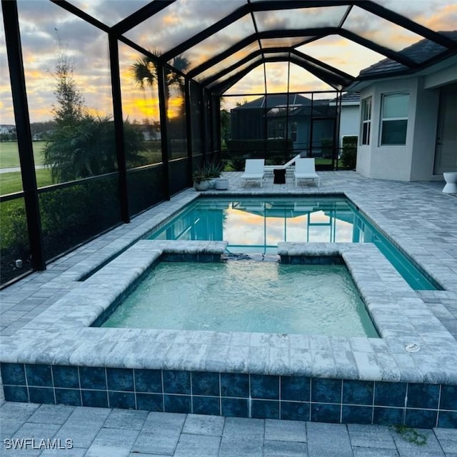 pool at dusk featuring an in ground hot tub, glass enclosure, and a patio area