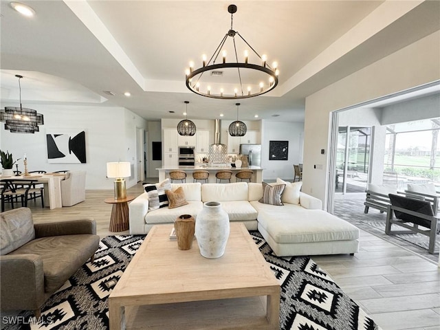 living room with light wood-type flooring, an inviting chandelier, and a tray ceiling