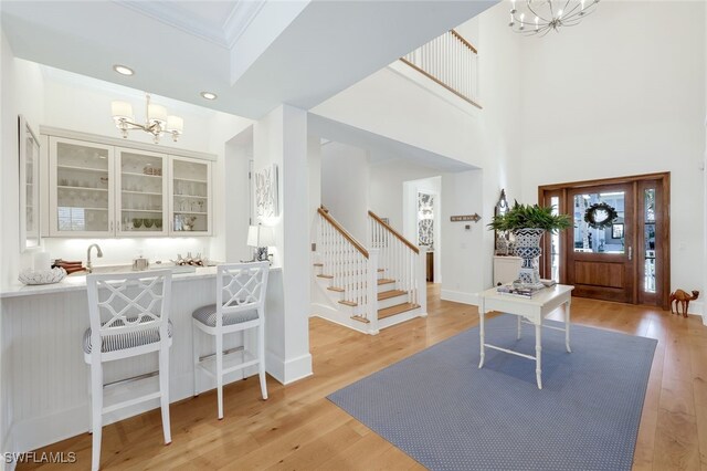 foyer entrance with a high ceiling, light wood-type flooring, crown molding, and an inviting chandelier