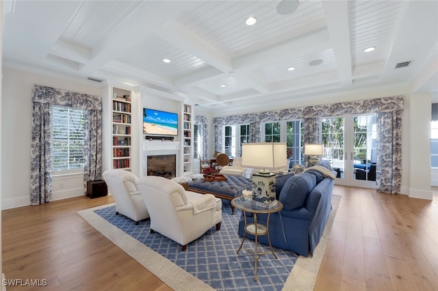 living room with built in shelves, ornamental molding, beamed ceiling, and light wood-type flooring