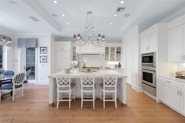 kitchen with stainless steel appliances, white cabinetry, hanging light fixtures, and an island with sink