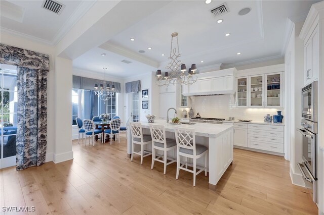 kitchen with white cabinetry, stainless steel appliances, an inviting chandelier, hanging light fixtures, and a kitchen island with sink