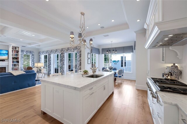 kitchen featuring pendant lighting, a center island with sink, sink, white cabinetry, and stainless steel gas cooktop