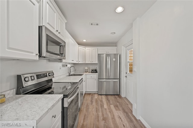 kitchen with light stone counters, stainless steel appliances, sink, light hardwood / wood-style flooring, and white cabinetry