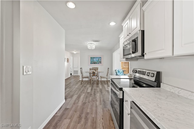 kitchen with white cabinets, appliances with stainless steel finishes, light wood-type flooring, and light stone counters