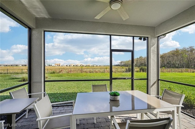 sunroom featuring ceiling fan and a rural view