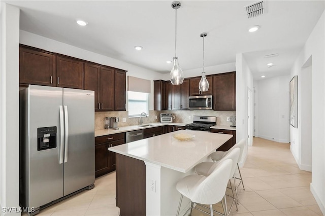 kitchen featuring a kitchen island, appliances with stainless steel finishes, decorative light fixtures, backsplash, and dark brown cabinets