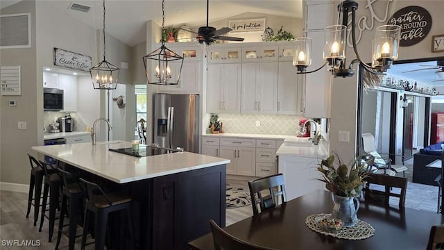 kitchen with a center island with sink, white cabinetry, appliances with stainless steel finishes, and ceiling fan with notable chandelier