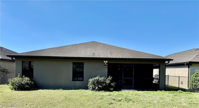 rear view of house with a shingled roof, stucco siding, a lawn, and fence