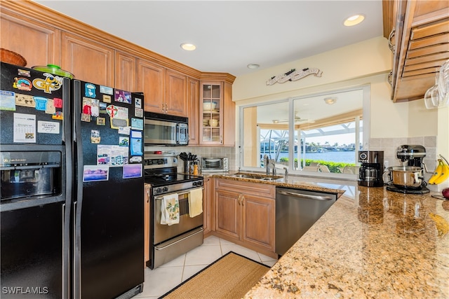 kitchen featuring light stone countertops, sink, stainless steel appliances, backsplash, and light tile patterned floors