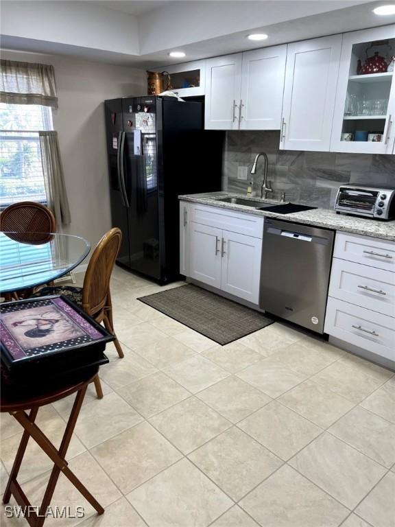 kitchen with a toaster, stainless steel dishwasher, freestanding refrigerator, white cabinetry, and a sink