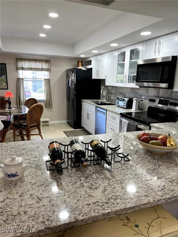 kitchen featuring a tray ceiling, stainless steel appliances, backsplash, a sink, and light stone countertops