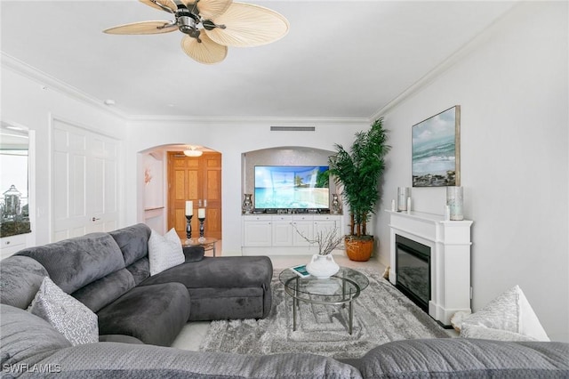 living room featuring visible vents, ceiling fan, ornamental molding, arched walkways, and a glass covered fireplace