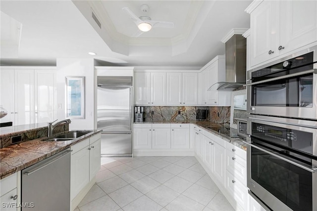 kitchen with visible vents, a tray ceiling, backsplash, appliances with stainless steel finishes, and wall chimney exhaust hood