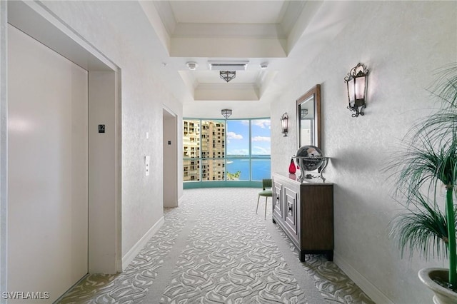 hall featuring crown molding, baseboards, a tray ceiling, elevator, and a textured wall