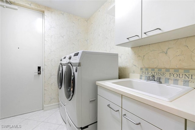 clothes washing area featuring a sink, cabinet space, separate washer and dryer, wallpapered walls, and light tile patterned floors