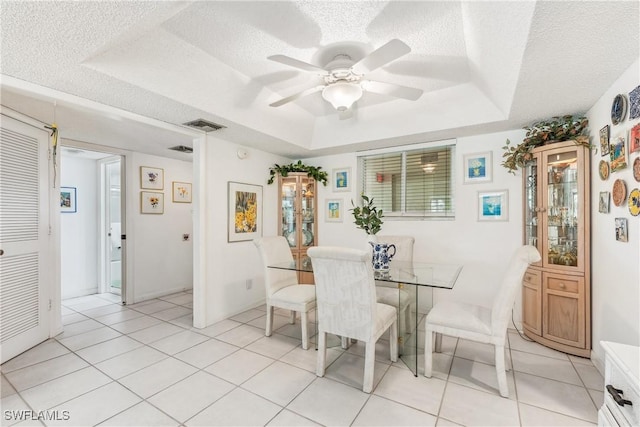 tiled dining area featuring a tray ceiling, a textured ceiling, and ceiling fan