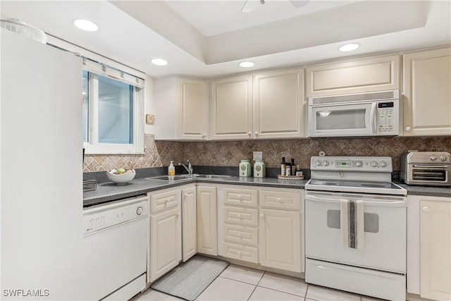 kitchen featuring sink, decorative backsplash, light tile patterned floors, a tray ceiling, and white appliances