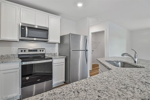 kitchen with light stone countertops, sink, stainless steel appliances, wood-type flooring, and white cabinets