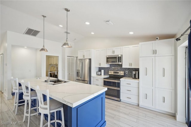 kitchen featuring stainless steel appliances, an island with sink, decorative backsplash, white cabinets, and sink