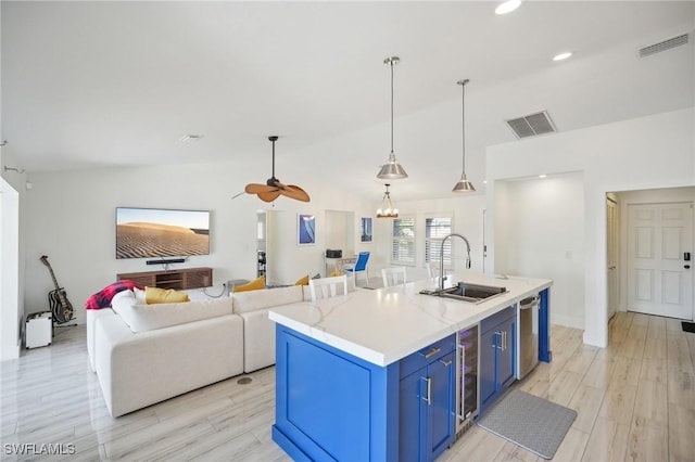 kitchen featuring stainless steel dishwasher, decorative light fixtures, a center island with sink, blue cabinetry, and sink