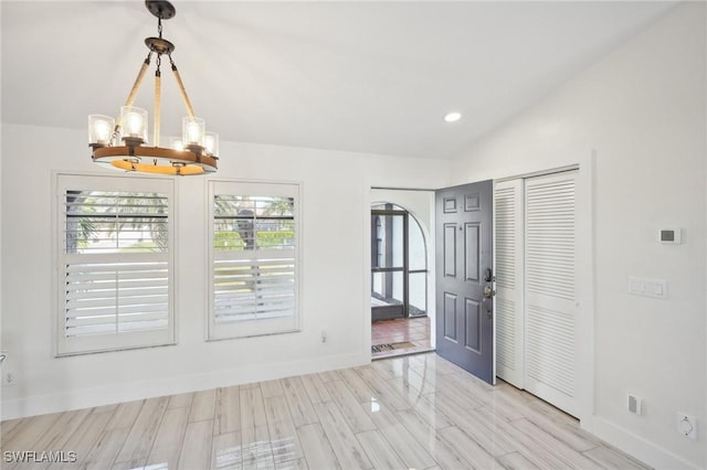 empty room featuring light wood-style floors, vaulted ceiling, baseboards, and an inviting chandelier