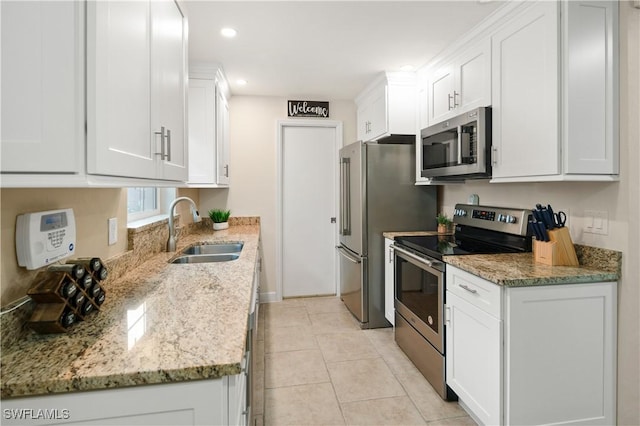 kitchen with white cabinets, appliances with stainless steel finishes, light stone counters, and sink