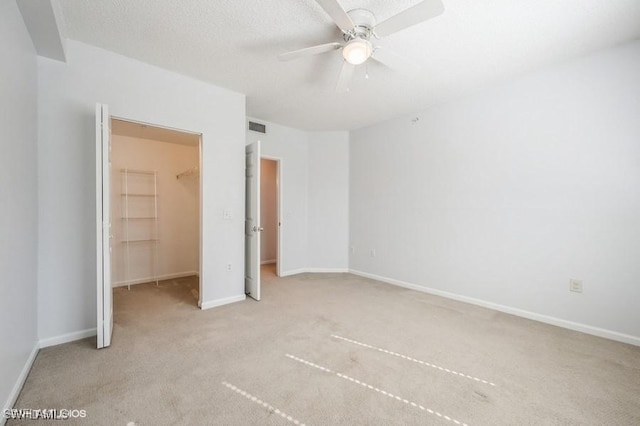 unfurnished bedroom with a walk in closet, ceiling fan, light carpet, a textured ceiling, and a closet