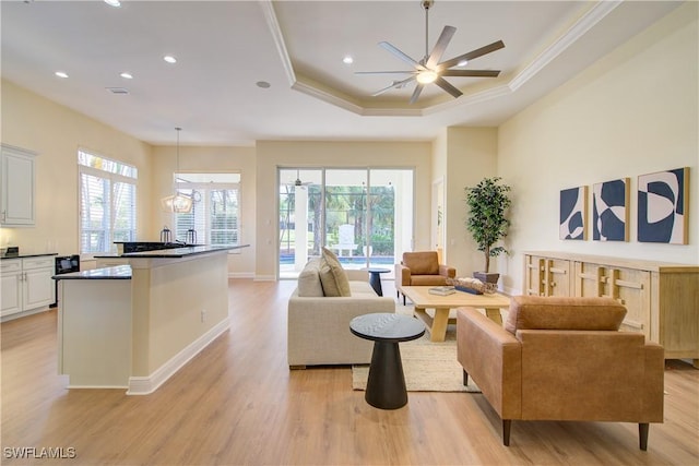 living room with a raised ceiling, ceiling fan, ornamental molding, and light wood-type flooring