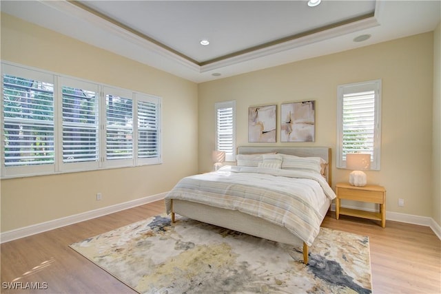 bedroom with a raised ceiling, light wood-type flooring, and crown molding