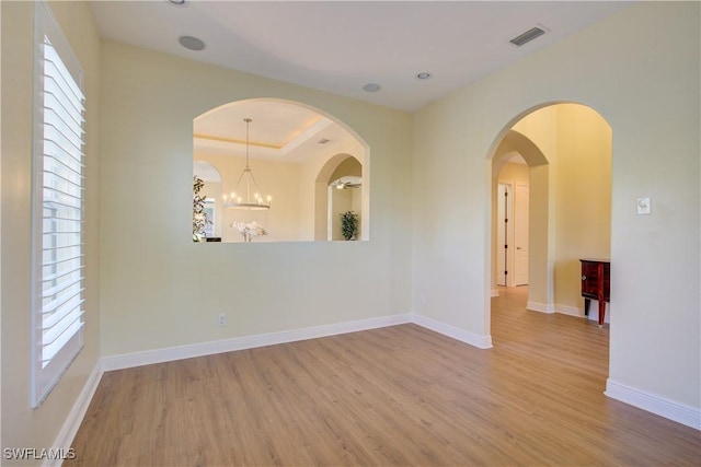 empty room with a tray ceiling, light hardwood / wood-style floors, and an inviting chandelier