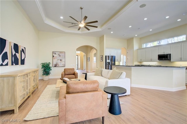 living room with a high ceiling, light hardwood / wood-style floors, a raised ceiling, and ceiling fan