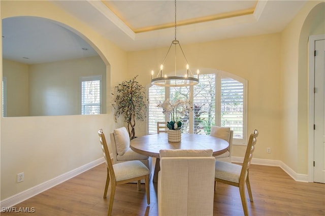 dining area featuring light hardwood / wood-style flooring, a raised ceiling, and a notable chandelier