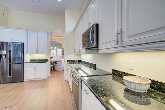 kitchen featuring white cabinets, light wood-type flooring, stainless steel appliances, and dark stone counters