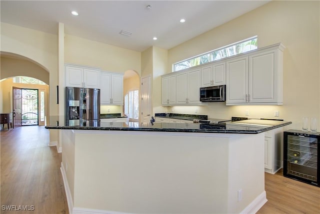 kitchen with beverage cooler, dark stone countertops, white cabinetry, and appliances with stainless steel finishes