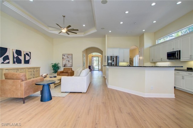 living room with ceiling fan, a high ceiling, light hardwood / wood-style floors, a tray ceiling, and ornamental molding